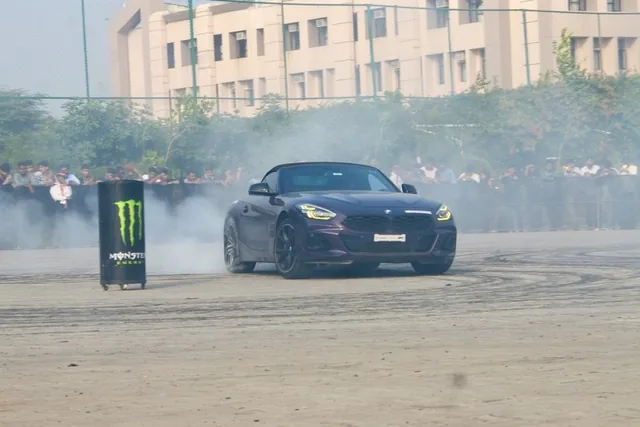 A dark BMW Z4 M40i drifting through tyre smoke in front of a crowd