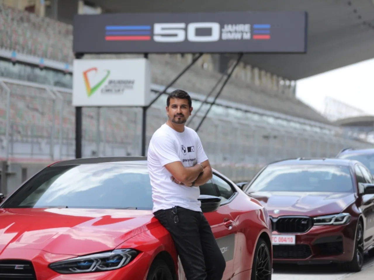 Nachiket Kulkarni, arms crossed, leaning on a red BMW at Buddh International Circuit
